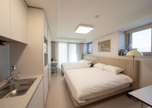 A hotel room with a kitchenette, two beds, a desk, and a window with a view. - UH FLAT THE SOKCHO (Sokcho)