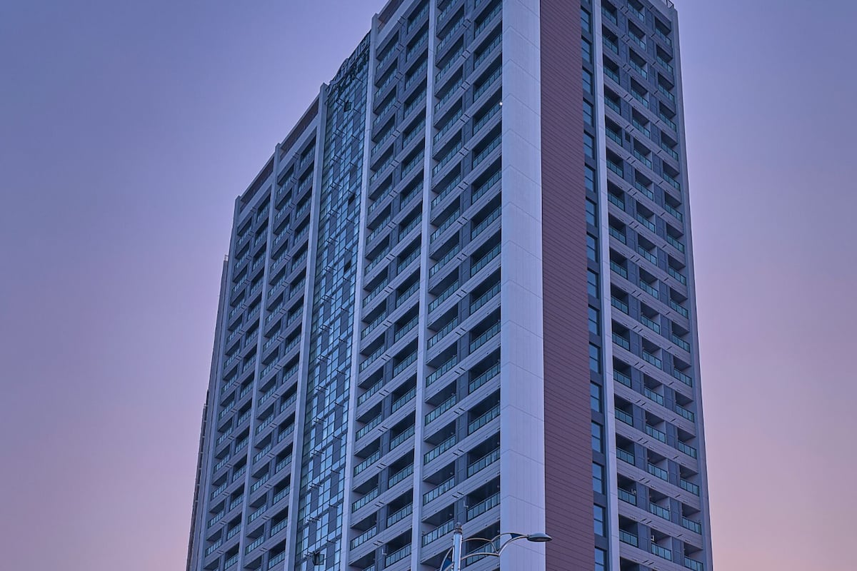 A tall, modern building with a grid of windows and a prominent vertical section in a contrasting color.