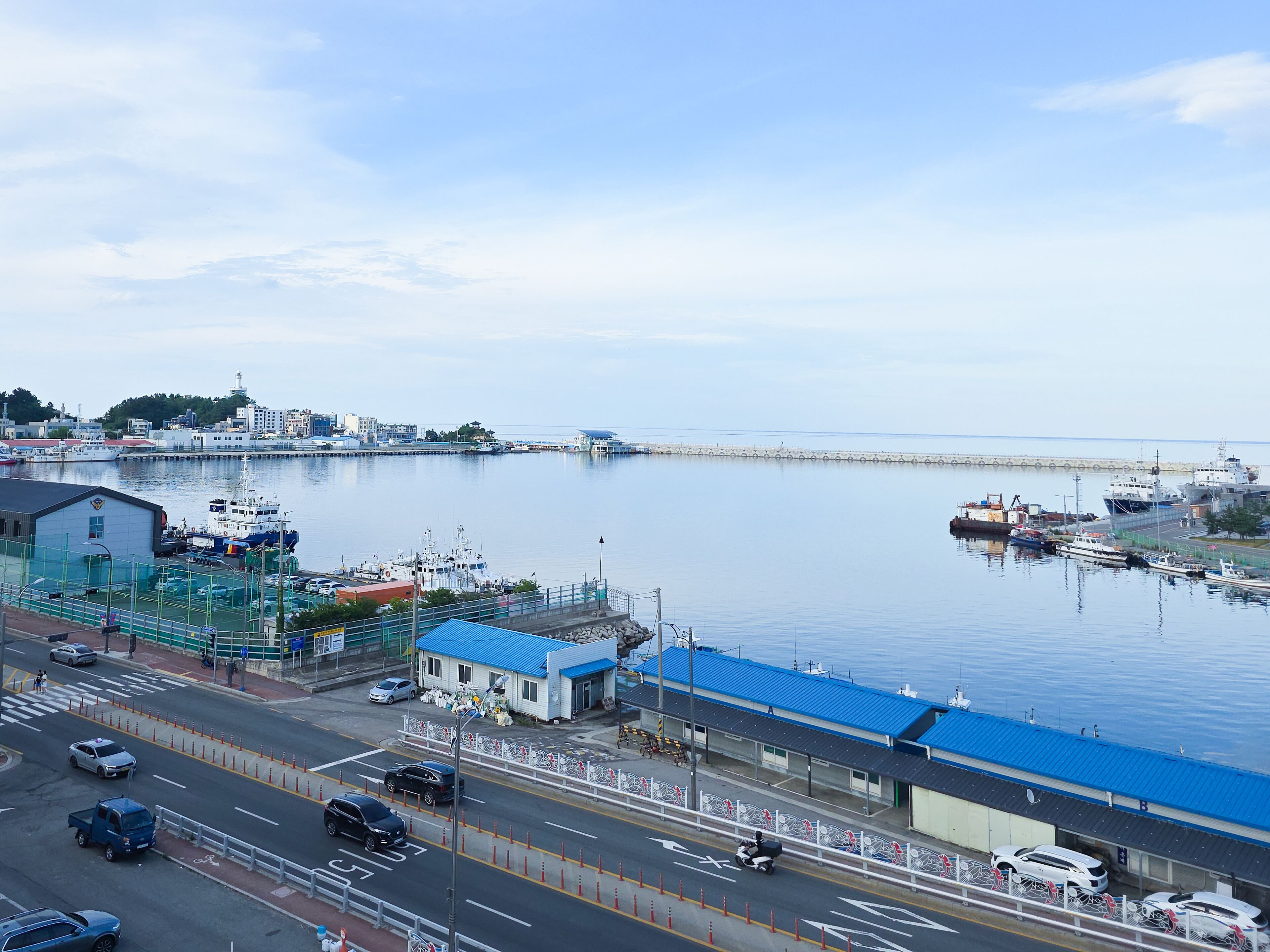 Une ville côtière dotée d’un port de plaisance, d’une route où circulent des véhicules et d’immeubles aux toits bleus.