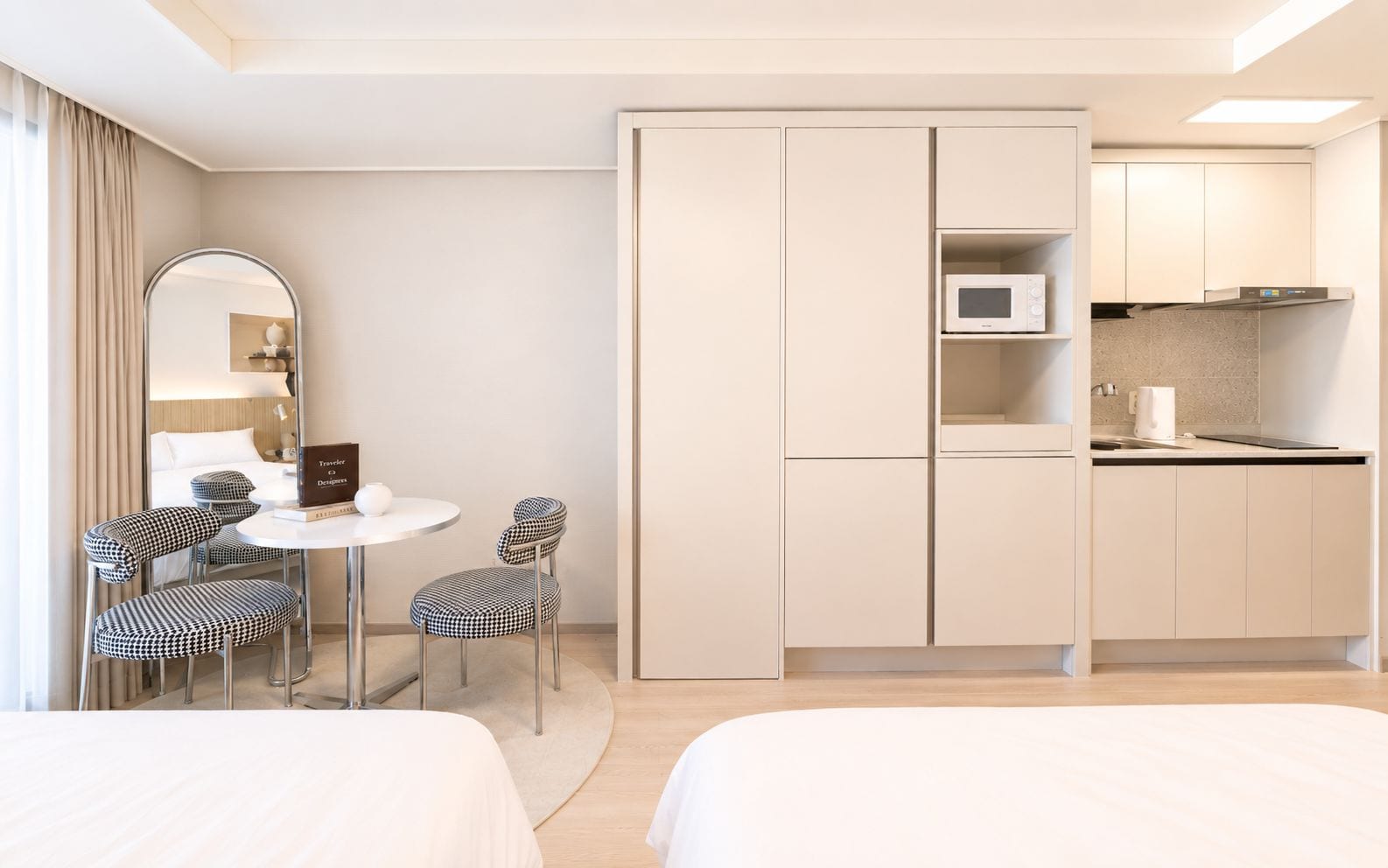 A hotel room with a bed, a desk with two chairs, a mirror, a kitchenette with a microwave, and a cabinet.