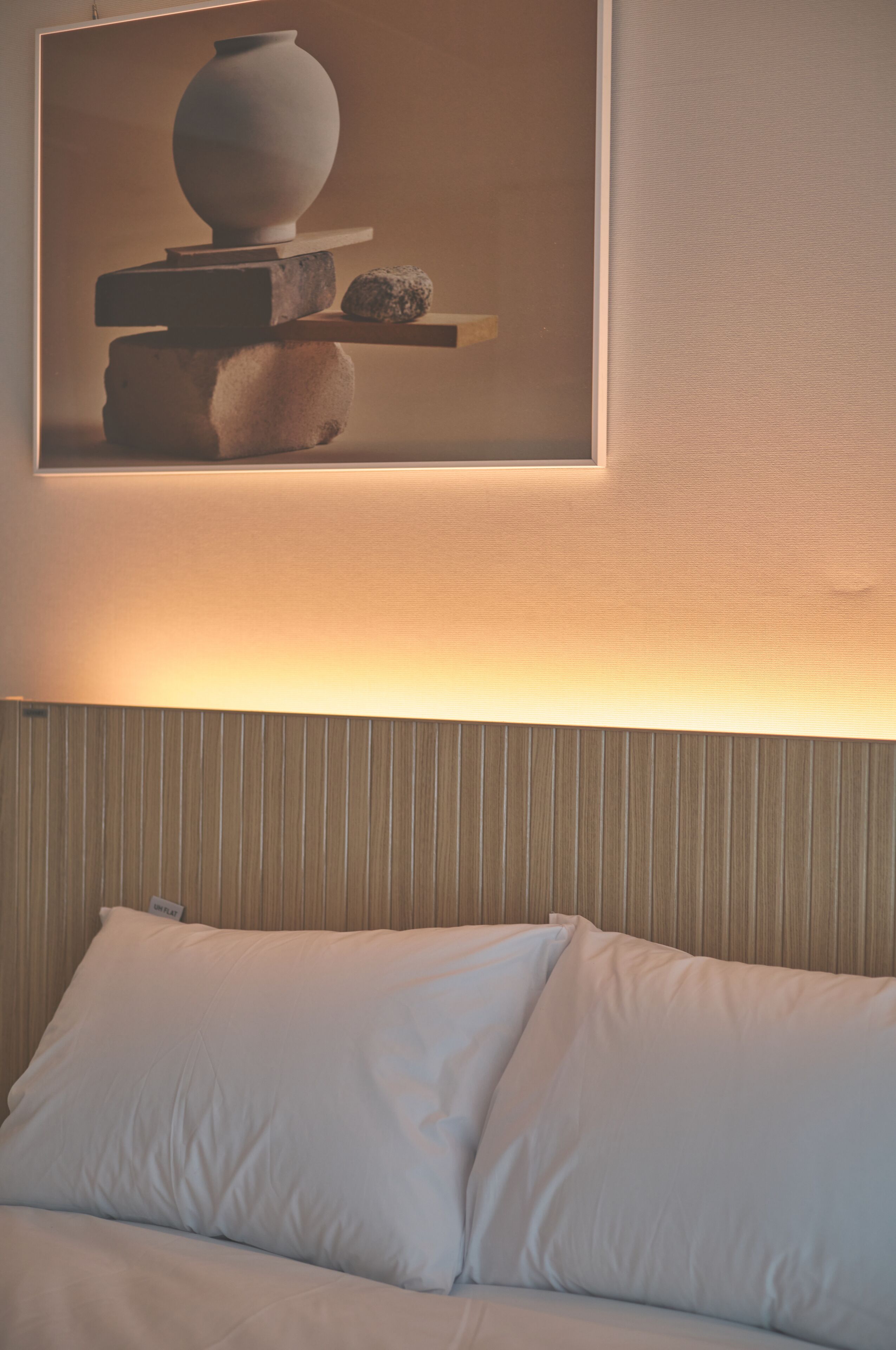 A hotel room with a bed, pillows, a framed artwork above the bed, and a textured wall.