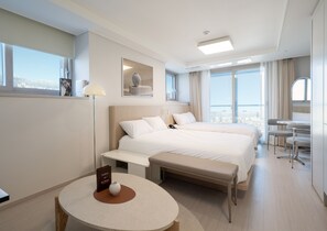 A hotel room with two beds, a round table with a vase, a bedside lamp, and a view of the city. - UH FLAT THE SOKCHO (Sokcho)
