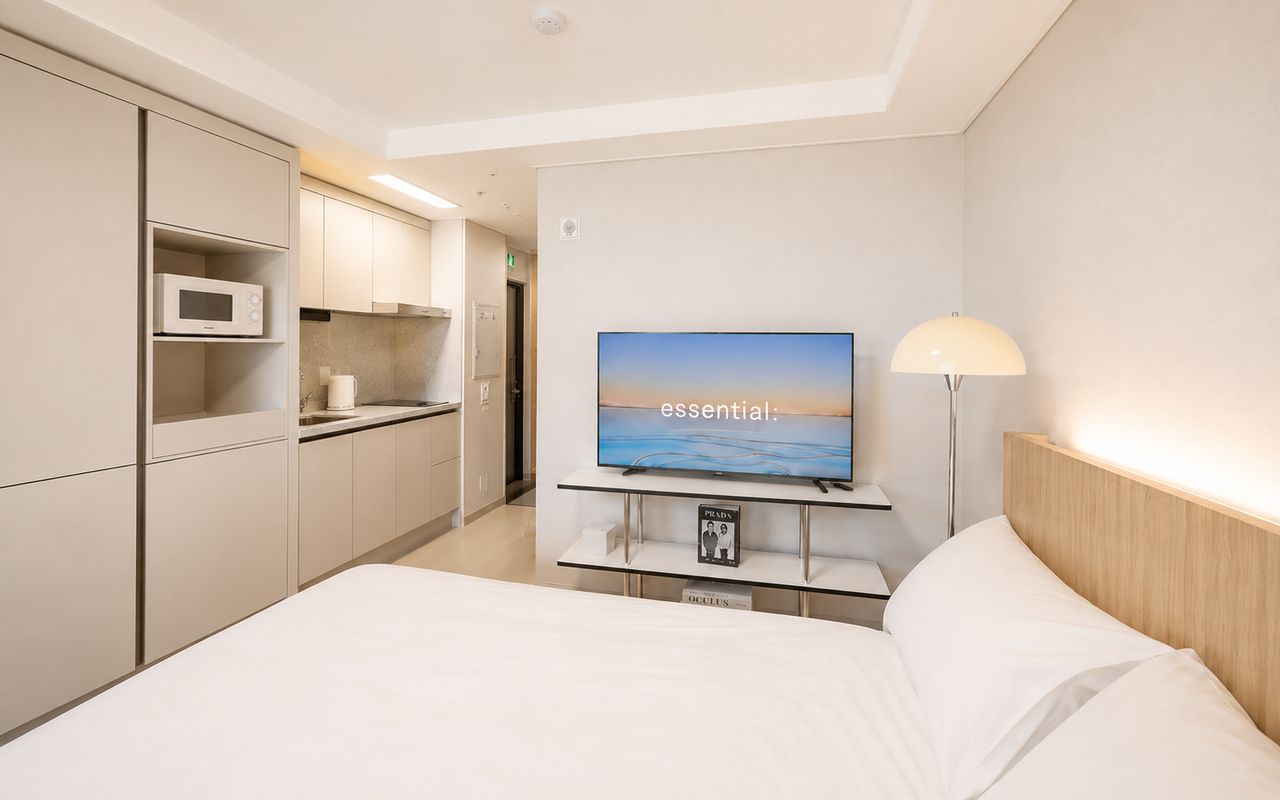 Una camera d'albergo con un letto, una TV su un mobile, un forno a microonde, una macchina per il caffè e una lampada.