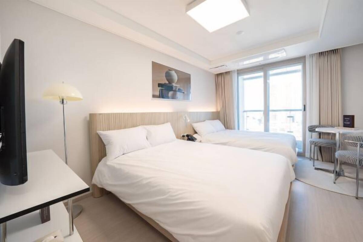 A hotel room with two beds, a desk, a chair, a TV, and a window with curtains.