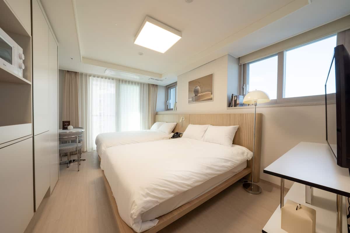 A modern hotel room with a large bed, a desk, a chair, a lamp, and a TV.