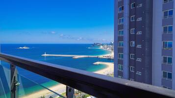 A high-rise building with balconies overlooking a coastal area, featuring a clear view of the beach and ocean.
