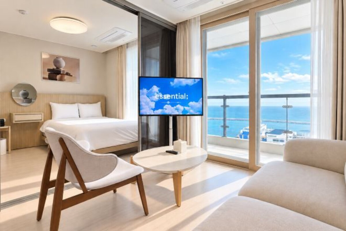 A hotel room with a bed, a TV, a balcony with a view of the sea, and a seating area.