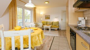 A compact kitchen with a dining area, a sofa, and a table set with yellow tablecloths. - Eickhus Weisse Wohnung by Interhome (Zinnowitz)