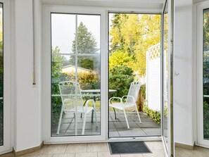 Una stanza con una porta scorrevole in vetro che dà su un patio esterno con sedie e tavolo in metallo bianco.