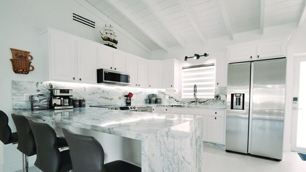 A modern kitchen with a large marble island, stainless steel appliances, and black bar stools. - Waterfront Marathon Retreat ,Private Boat Dock & Lift ,Hot Tub ,Sleeps 8 (Marathon)