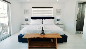 A modern bedroom with a large bed, bedside tables, a wooden coffee table, and a view of the outside. - Waterfront Marathon Retreat ,Private Boat Dock & Lift ,Hot Tub ,Sleeps 8 (Marathon)