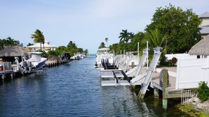 A marina with boats docked along a narrow waterway, surrounded by palm trees and thatched-roof structures. - Waterfront Marathon Retreat ,Private Boat Dock & Lift ,Hot Tub ,Sleeps 8 (Marathon)