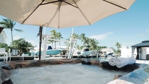 A hot tub area with a large umbrella, surrounded by palm trees and a pool. - Waterfront Marathon Retreat ,Private Boat Dock & Lift ,Hot Tub ,Sleeps 8 (Marathon)