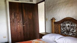 A bedroom with a wooden door, a bed with a patterned bedspread, and a nightstand. - Finca-Hostal Sanfelipe (Calima)