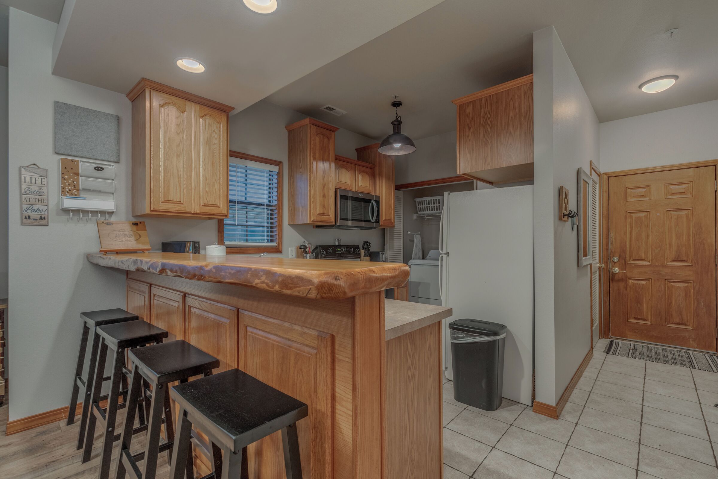 A kitchen with wooden cabinets, a central island with stools, a microwave, and a refrigerator.