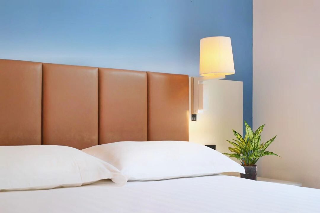 Ein Hotelzimmer mit braunem Kopfteil, weißer Bettdecke und einer Nachttischlampe.
