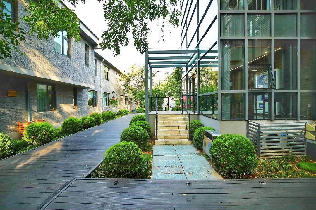 A modern building with a covered walkway, steps leading to a glass entrance, and a wooden deck.
