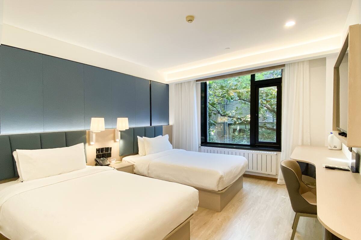 Habitación de hotel con dos camas, un escritorio y una ventana que da a zonas verdes.