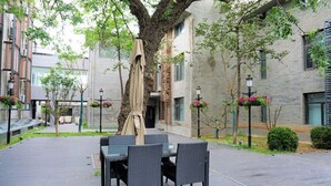 An outdoor patio with a table and chairs, surrounded by trees and a building with a brick facade. - Hotel Yoo Beijing  (Beijing)