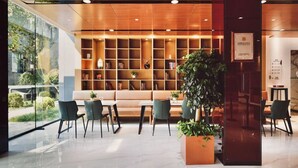A modern reception area with a wooden reception desk, a seating area with a sofa and chairs, a large potted plant, and a bookshelf filled with books. - Hotel Yoo Beijing  (Beijing)