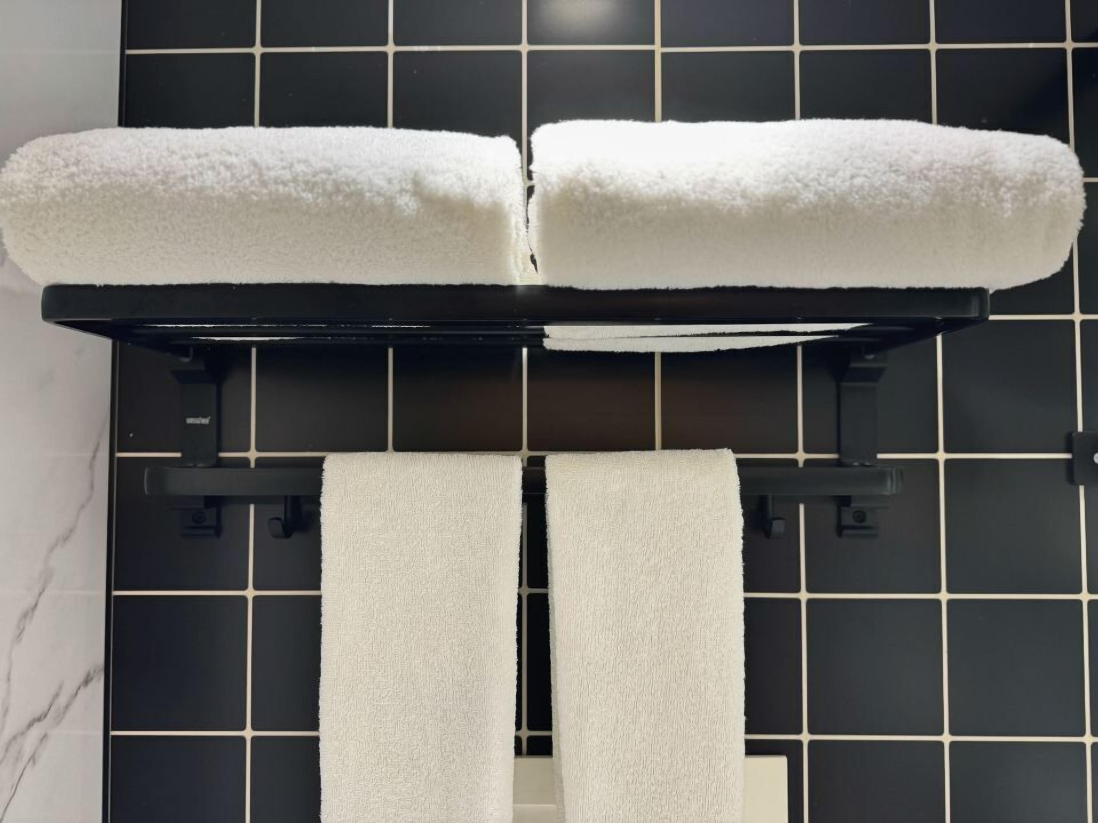 Ein Badezimmer mit schwarzen Fliesenwänden, einem weißen Handtuchhalter und zwei weißen Handtüchern.
