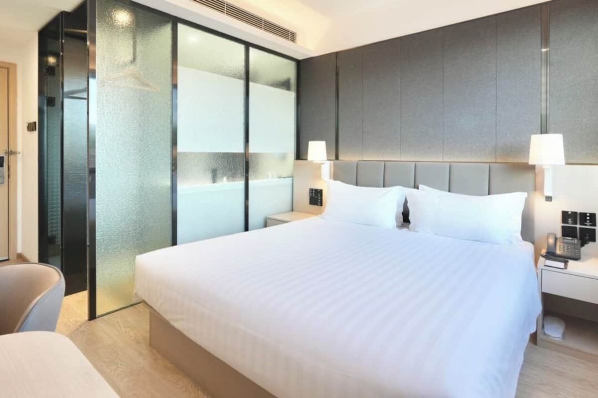 Una habitación de hotel moderna con una cama grande, dos lámparas de noche, una mesita de noche y un mamparo de vidrio.
