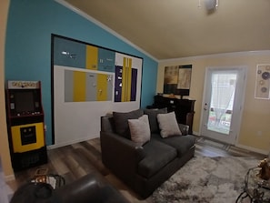 Una sala de estar con un sofá gris oscuro, un reloj en la pared y una máquina de videojuegos Pac-Man.