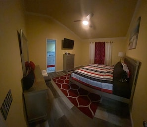 Un dormitorio con cama, cómoda, televisor y ventilador de techo.