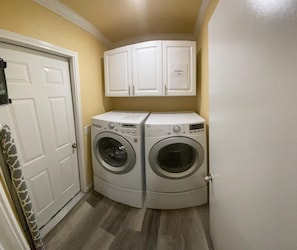 A laundry room with two front-loading washing machines, a white door, and a cabinet above the machines.