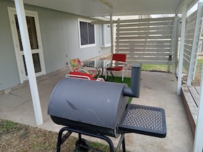 Un patio al aire libre con una parrilla, una silla roja y una mesa.