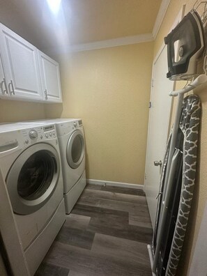 A laundry room with two front-loading washing machines, a dryer, and a ceiling-mounted iron. - Charming 3 Bed 2 Bath Home in NE San Antonio (Converse)