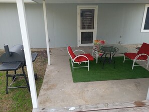 An outdoor patio with a grill, a table, and red chairs.