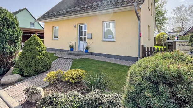Ein zweistöckiges Haus mit einem Ziegeldach, einer Haustür und einer kleinen Veranda mit Blumentöpfen.