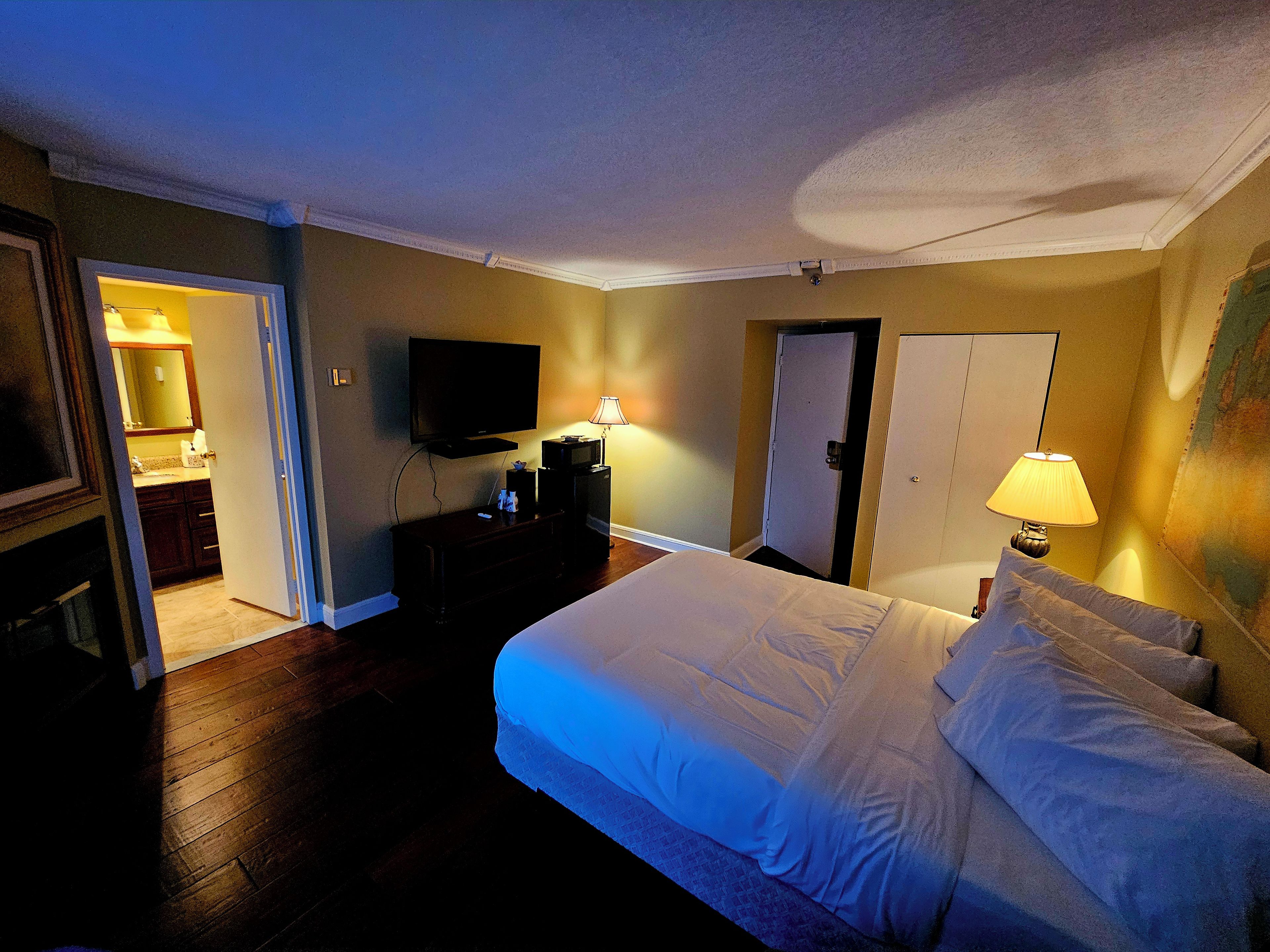 A hotel room with a bed, a television, a desk with a lamp, a wardrobe, and a bathroom visible through an open door.