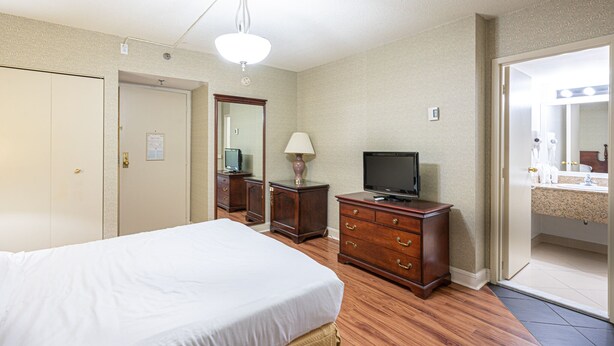 Habitación de hotel con una cama, televisor, cómoda y baño visible a través de una puerta abierta.