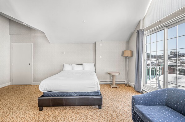 A hotel room with a large bed, a small round table, a sofa, and a view of a snowy landscape through the window.