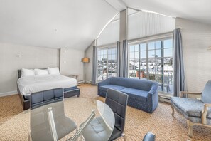 A hotel room with a large bed, a sofa, a chair, a small table, and a large window with a view of the city.