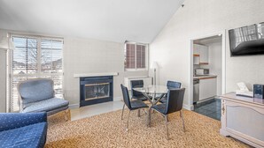 Una sala moderna con chimenea, una mesa de comedor con sillas, un sofá y una cocina visible a través de una puerta abierta.