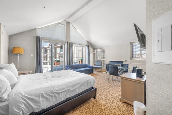 A hotel room with a large bed, a desk, a chair, and a sofa. There is a window with curtains, a lamp, and a TV on the wall. - Hotel le Domaine Studio Queen kitchen balcony (Saint-sauveur)