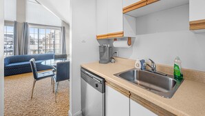 Una cocina moderna con lavavajillas, cafetera y pileta. Hay un comedor con un sofá azul y sillas.