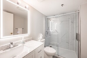 Ein modernes Badezimmer mit einer Glaskabine zur Dusche, einem Marmorwaschbecken und einem großen Spiegel mit integrierter Beleuchtung.