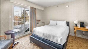 A hotel room with a bed, a small table, a chair, a desk with a lamp, and a view of the outdoors through a large window.