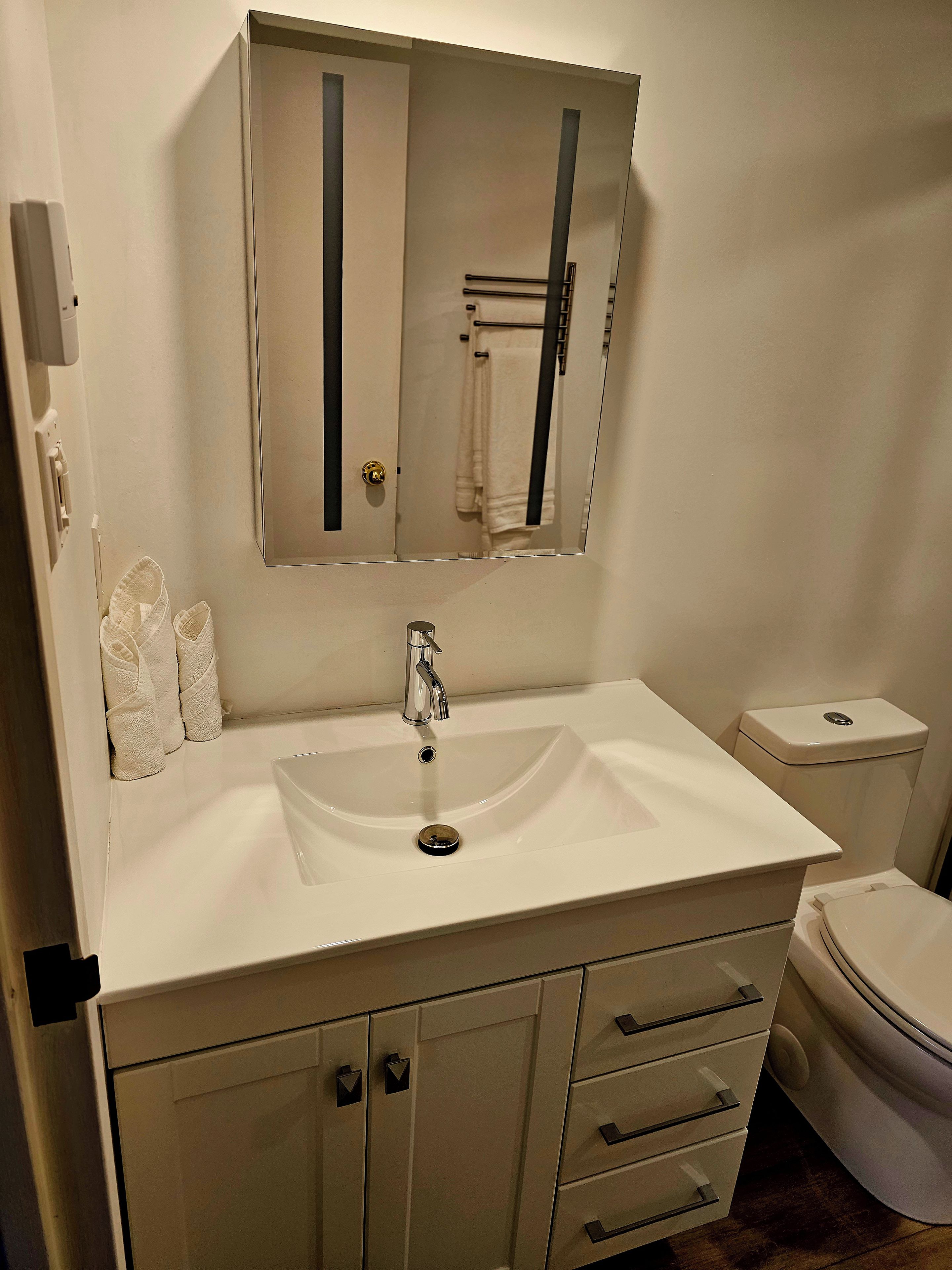 A bathroom with a white sink, a mirror, a toilet, and a cabinet with drawers.