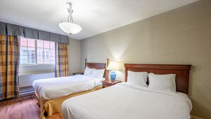 A hotel room with two single beds, wooden headboards, a bedside table with a lamp, and a window with curtains.