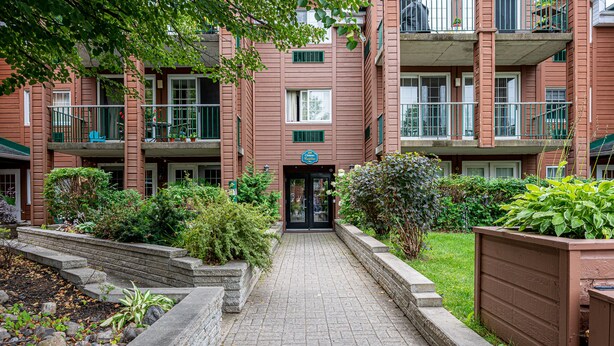 A brick building with a central entrance, surrounded by a garden with various plants and a paved walkway.