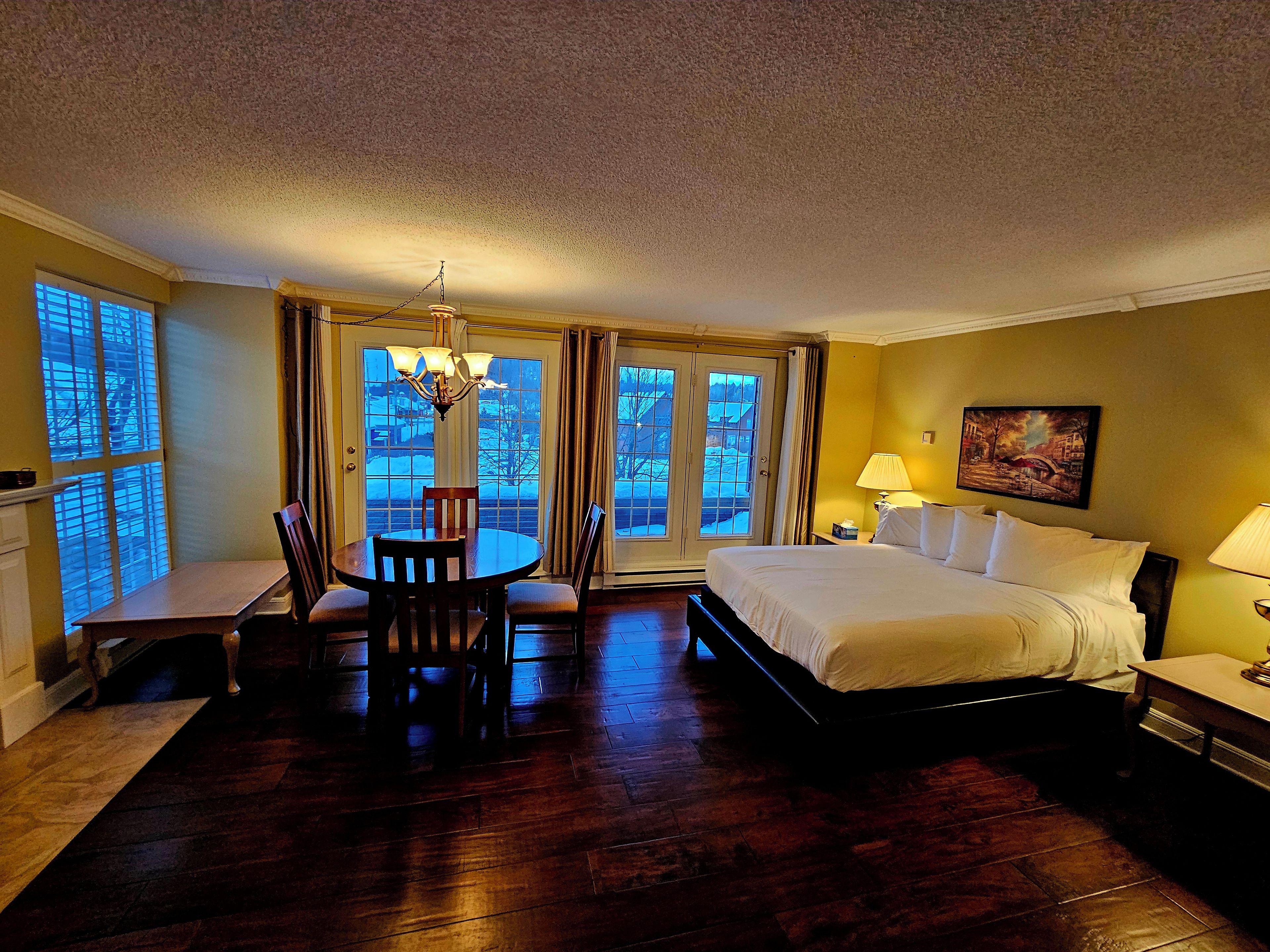 A hotel room with a bed, a dining table with chairs, a chandelier, and a painting on the wall.