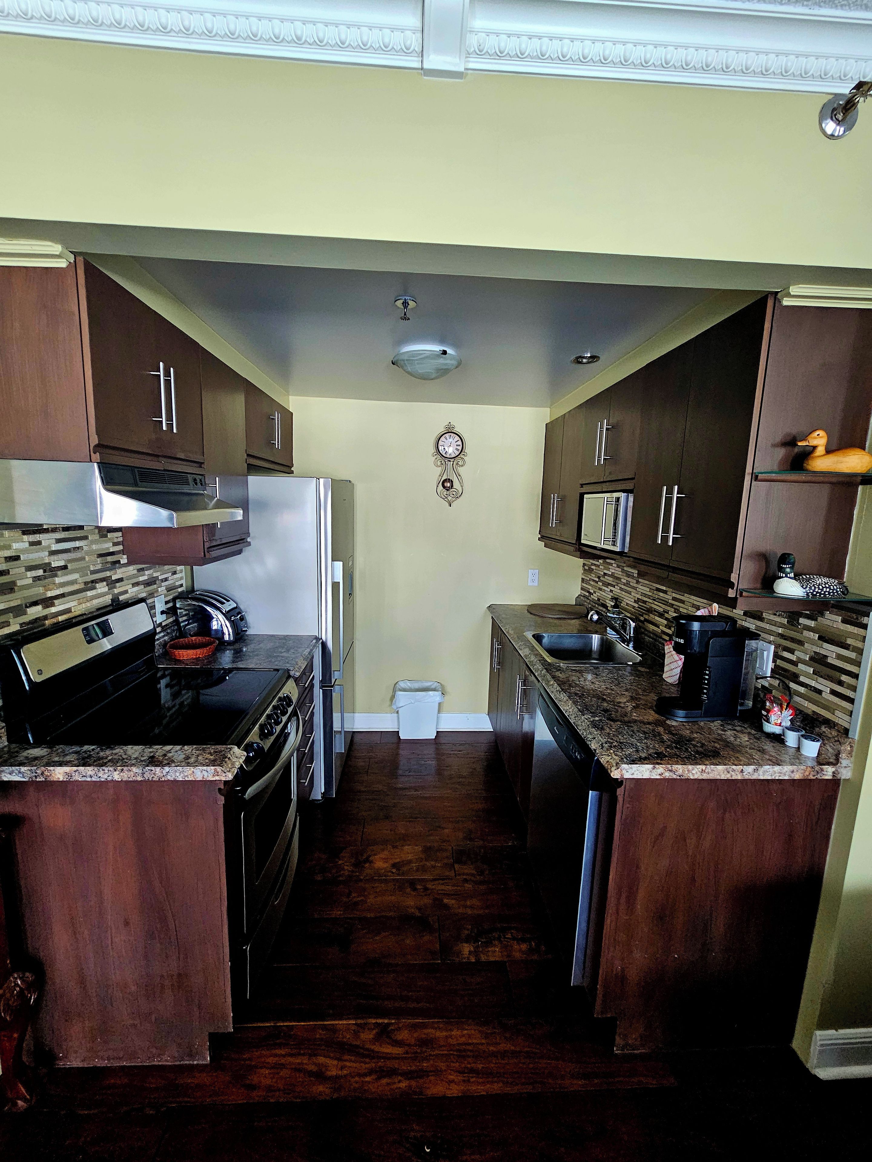 A compact kitchen with dark wood cabinets, a stainless steel range hood, a built-in oven, a microwave, and a coffee maker.