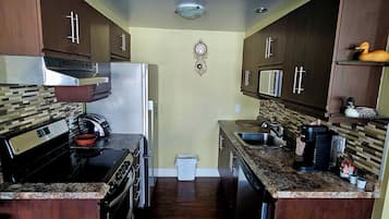A compact kitchen with dark wood cabinets, a stainless steel range hood, a built-in oven, a microwave, and a coffee maker.