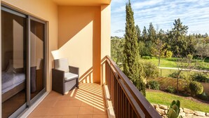 A balcony with a sofa and a chair, a glass door, and a view of a green landscape with trees and a fence. - Triplex Vilamoura VIP Properties by Interhome (Vilamoura)