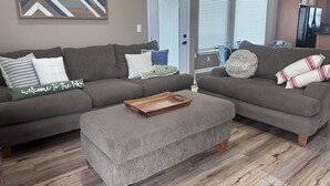 Ein Wohnzimmer mit einem Ecksofa, einem Holztisch und einer Wanddekoration.